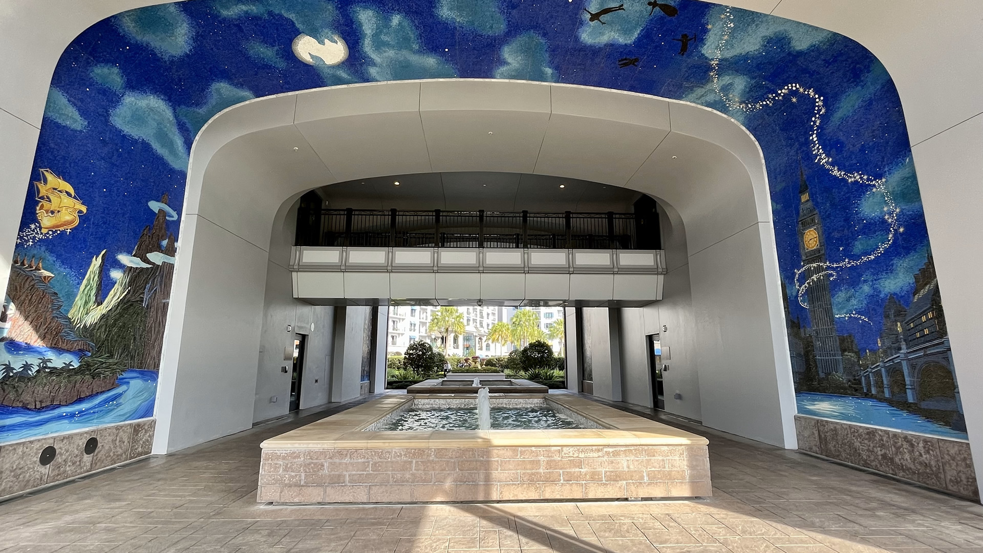 A large mosaic depicting Peter Pan and the Darling children flying through the night sky over the London skyline to Neverland covers the walls and ceiling over a fountain and walkway into Disney’s Riviera Resort.