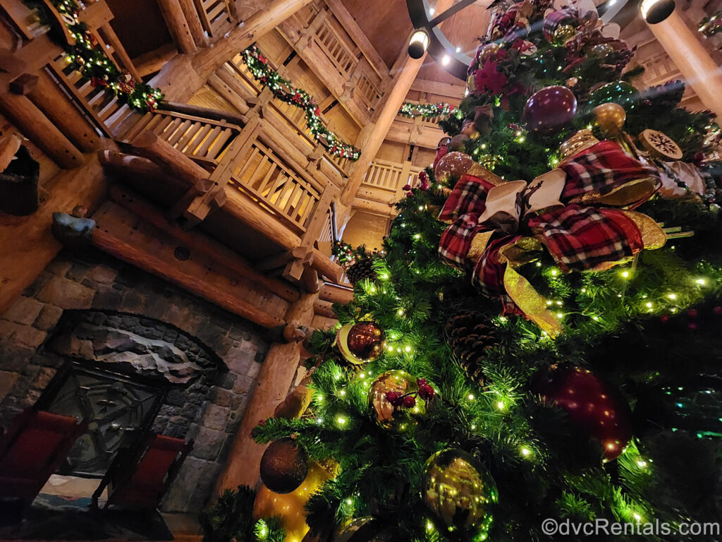 A green Christmas tree with red, gold, and wooden ornaments and white lights along with matching garlands decorate the log cabin-style lobby space of the Boulder Ridge Villas at Disney’s Wilderness Lodge.