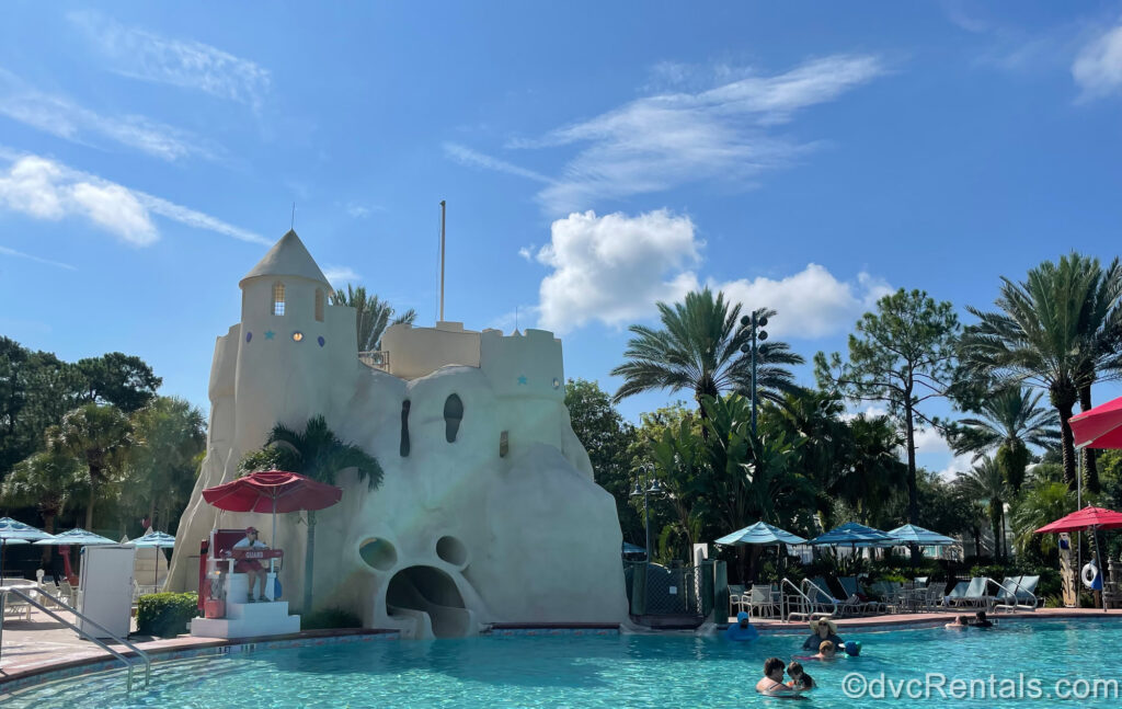 The Sandcastle Pool at Disney’s Old Key West Resort is seen on a sunny day. There is a large beige structure made to look like a giant sandcastle that holds the waterslide, and the opening is shaped like Mickey Mouse’s head.