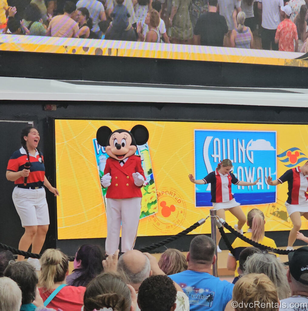 Minnie Mouse in a red and white nautical-inspired suit outfit performs for guests with Disney Cast Members in the Sailing Away party.