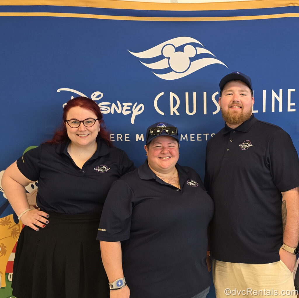 David’s Vacation Club Rentals team members Kristen, Lindsay, and Nick pose in front of a navy blue Disney Cruise Line banner.