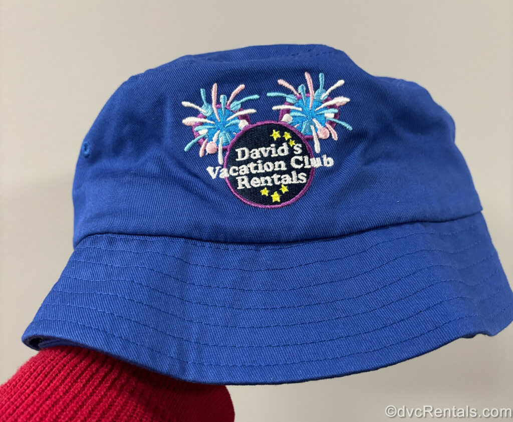 A royal blue bucket hat features the navy-blue David’s Vacation Club Rentals logo along with yellow stars and blue, pink, and purple fireworks embroidered on it.