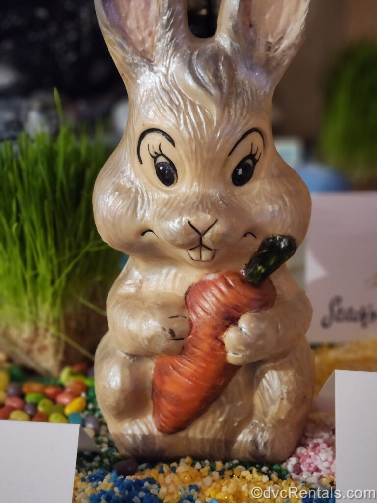 A shimmery beige Easter bunny made of chocolate holding a small orange carrot is on display at EPCOT.