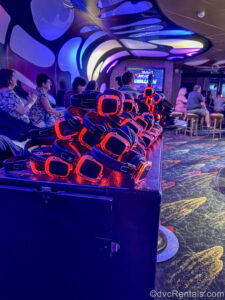 The light-up headphones are in a pile ready for the Silent Disco event onboard the Disney Dream. Guests participating in a trivia event are seen in the background.
