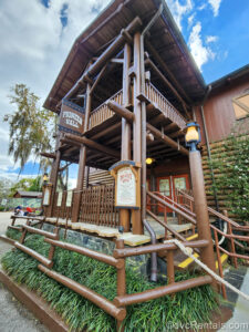 The frontier-inspired wooden exterior of Pioneer Hall at Disney’s Fort Wilderness is seen. There is a small sign on the front advertising the Hoop-Dee-Doo Musical Revue dinner show.