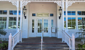 The staircase leading to the white exterior entrance to Gasparilla Island Grill is seen. There is a menu board outside displaying photos of some items.