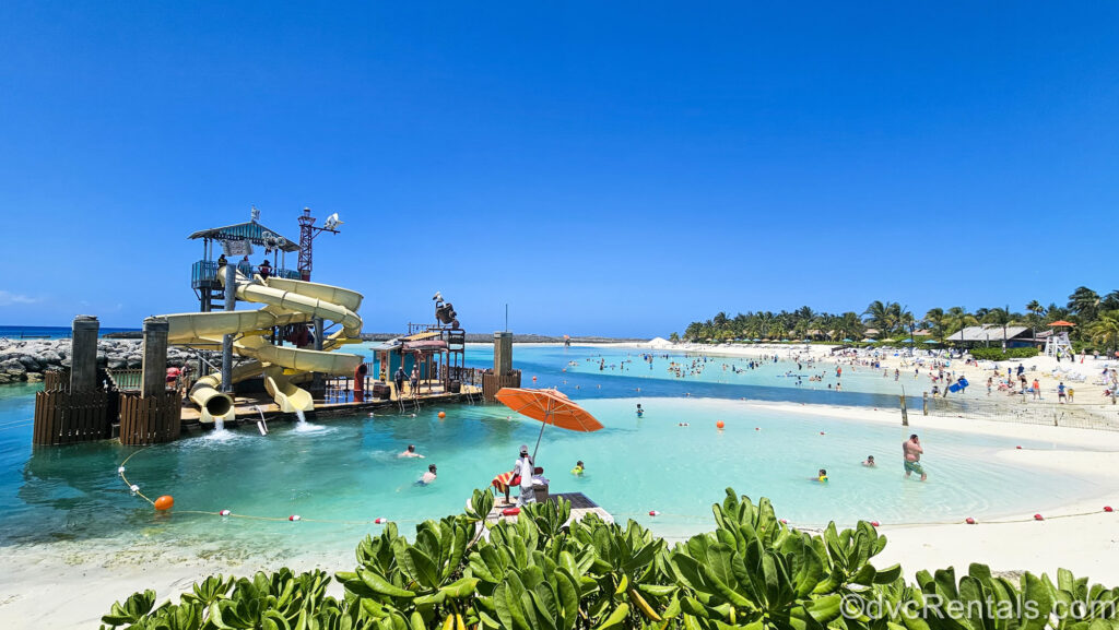 Guests enjoy the Pelican Plunge waterslides, ocean waters, and beaches at Disney Castaway Cay under a sunny sky.