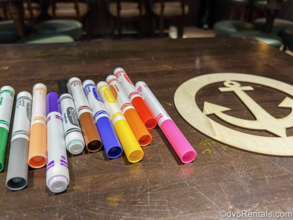 Several colorful markers sit next to a wooden anchor decoration to be decorated during an arts & crafts event during a day at sea aboard the Disney Fantasy.
