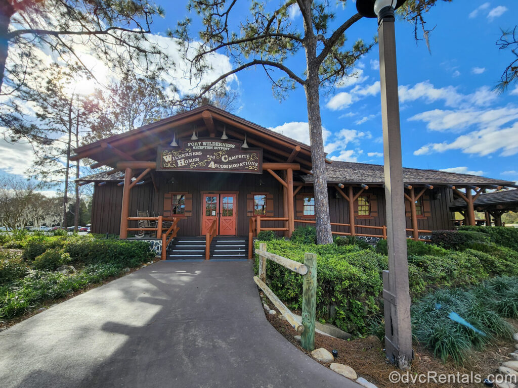 The dark brown log-cabin style exterior of the reception area at Disney’s Fort Wilderness Resort is seen under a sunny sky, surrounded by green foliage.