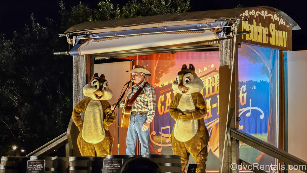 Chip ‘n’ Dale and their cowboy friend perform a campfire sing-along on a stage made from an old-fashioned covered wagon at night at Disney’s Fort Wilderness Resort.
