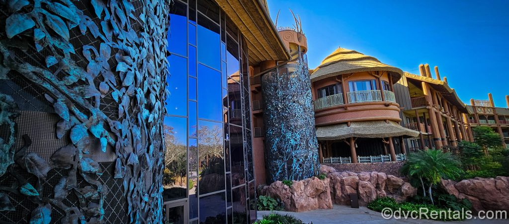 The African-inspired exterior buildings and foliage of Disney’s Animal Kingdom Villas Jambo House are seen under a sunny blue sky.