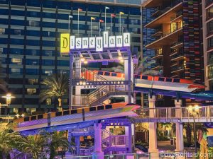 Two Monorail decorations and the retro Disneyland sign are seen overlooking the waterslide featured at the Villas at Disneyland Hotel at night as the lights glow over the pool area.