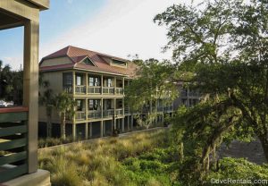 The green and brown exterior buildings of Disney’s Hilton Head Island Resort are seen amongst the green foliage of the grounds.