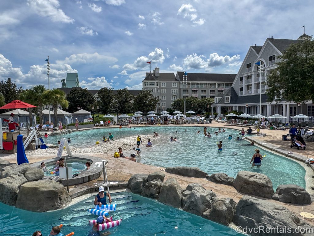 Guests at Disney’s Beach Club Villas enjoy the sand, pool, hot tub, and loungers at the Stormalong Bay pool under a sunny sky.