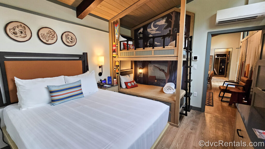 The bedroom of a DVC Cabin at Disney’s Fort Wilderness Resort. There is a queen bed with twin bunk beds next to it. Above each bed is nature-themed artwork featuring Chip ‘n’ Dale.