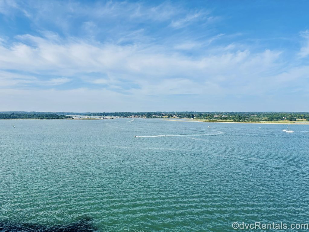The waters of the English Channel, smaller watercrafts, and green fields outside Southampton, England are seen under a blue sky from onboard the cruise ship.