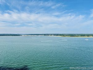 The waters of the English Channel, smaller watercrafts, and green fields outside Southampton, England are seen under a blue sky from onboard the cruise ship.