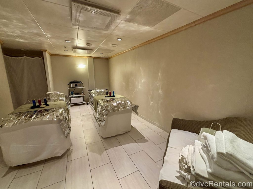 Two massage tables arranged with skincare supplies and silver foil are seen in a dimly lit treatment room of the Vitality Spa.