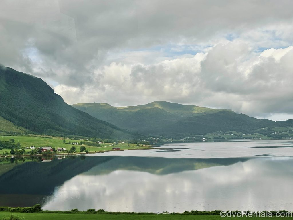 Scenic green fields and mountains are seen along the sides of the water under a cloudy sky near Molde, Norway.