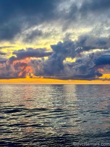 Shades of yellow, orange, pink, purple, and blue fill the sky as the sun begins to set just around midnight above the Norwegian fjords.