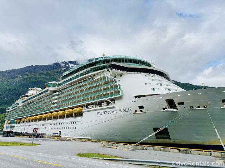 The exterior or Royal Caribbean’s Independence of the Seas is seen from the port of Olden, Norway, with mountains in the background under a cloudy sky.