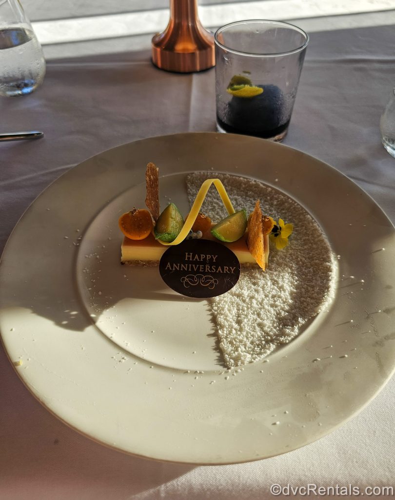The Citrus Bar dessert from ‘Ama’Ama at Aulani, a Disney Resort & Spa is served on a white plate with a chocolate piece reading “Happy Anniversary” on it.