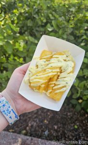 A hand holds a basket with a serving of Adobo Yuca Fries topped with garlic-cilantro aioli from the Fry Basket booth in it at the EPCOT International Food & Wine Festival.