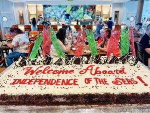 A large cake decorated with the words “Welcome Aboard Independence of the Seas!” in seen in front of guest tables at the Windjammer Marketplace buffet.