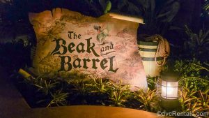 The exterior sign for The Beak and Barrel. The sign looks like an oversized, old, un-rolled map scroll and features a green parrot with an eye patch and pirate hat.