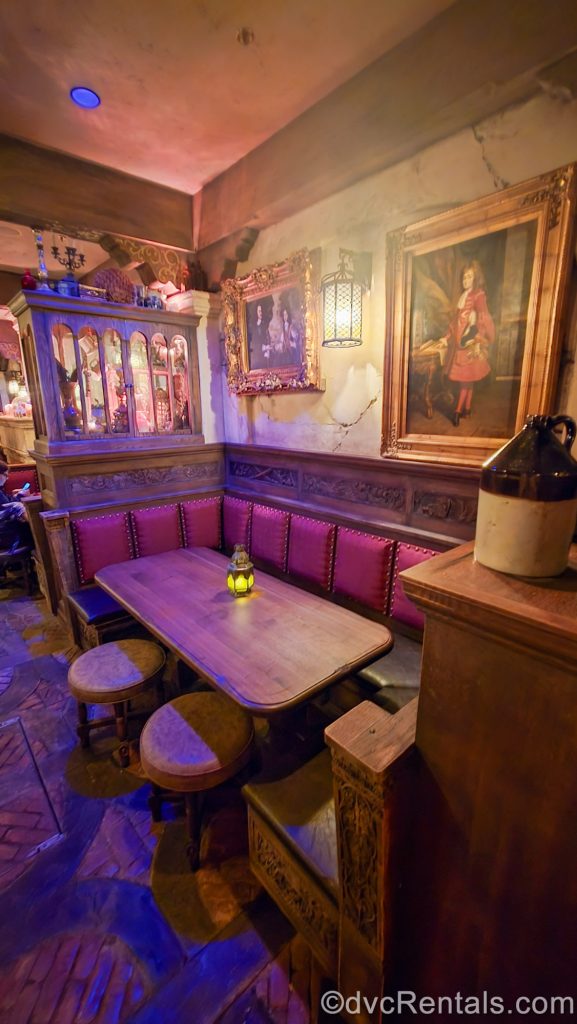A table with red and wood booth and stools sits awaiting guests to be seated amid old pirate-themed trinkets and portraits to view at The Beak and Barrel.