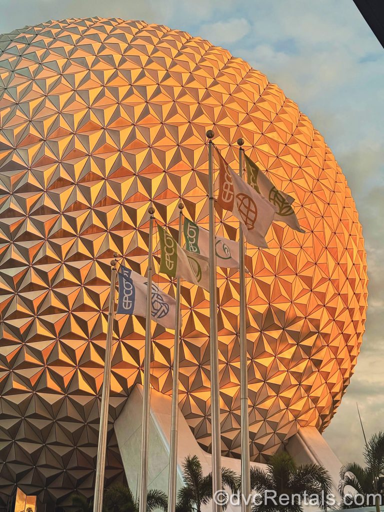 paceship Earth is lit with the warm glow of the golden hour sun at EPCOT as park flags wave in the foreground.