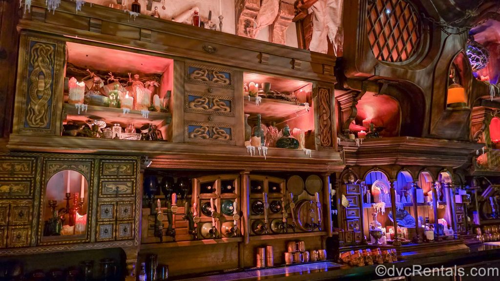 The shelving display behind the bar of the Beak and Barrel which is decorated with dripping candles, old bottles, wooden kegs, and other pirate-themed knickknacks.