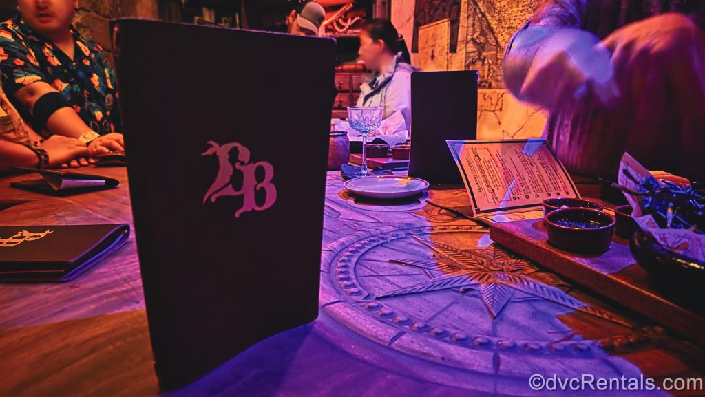 Menu books, plates, trays, and drinkware are seen on the communal table as guests enjoy their selections.