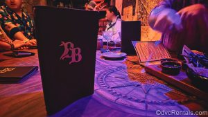 Menu books, plates, trays, and drinkware are seen on the communal table as guests enjoy their selections.