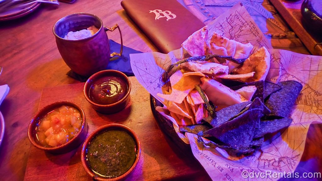 The Island Provisions plantain chips, corn tortillas, and toasted flatbread with assorted dips and the Cursed Treasure drink served in a copper mug.