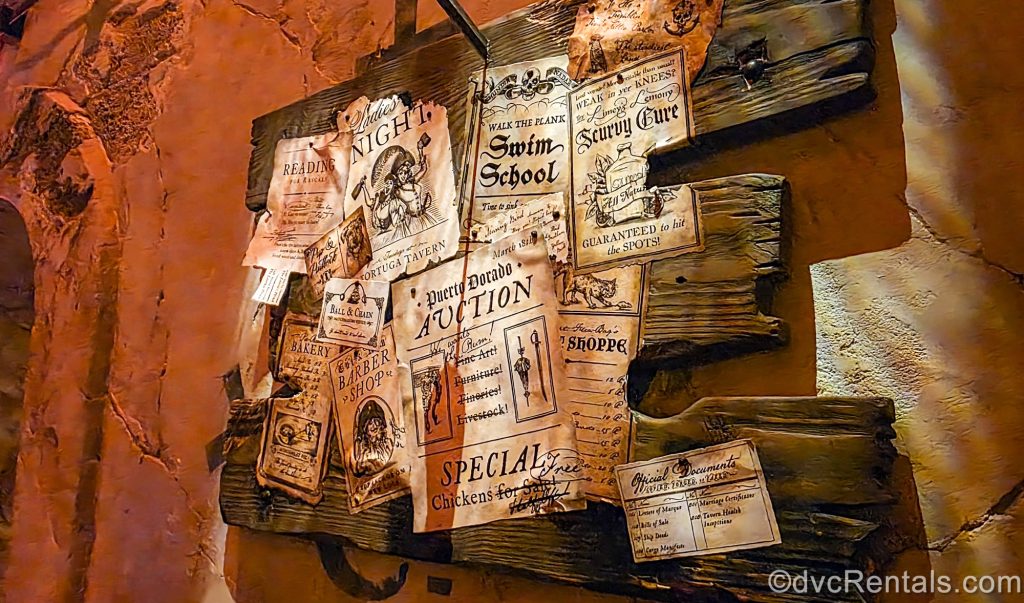 A bulletin board full of aged, satirical pages advertising pirate-themed events such as auctions and swimming classes is seen. They are heavily influenced by the Pirates of the Caribbean attraction.