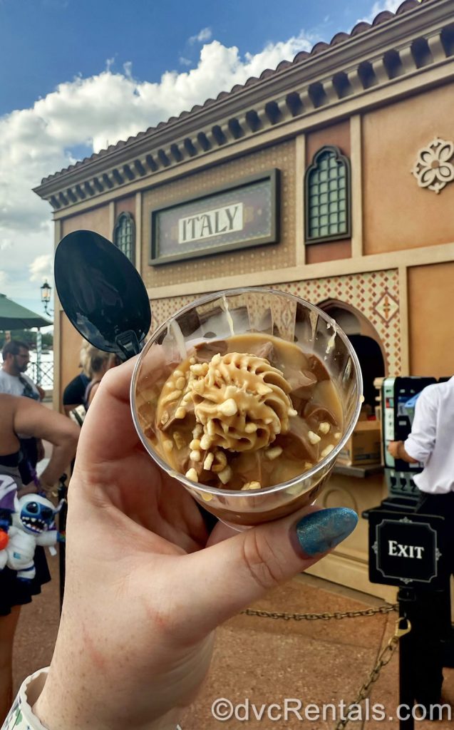 A hand holds up a serving of Chocolate Spuma in front of the Italy booth at EPCOT.
