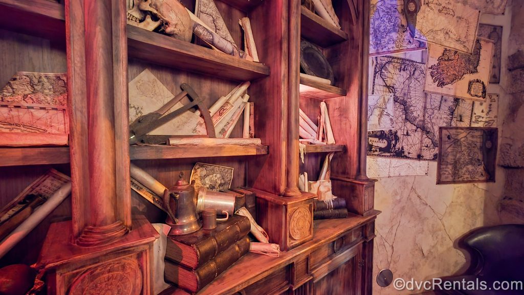Wooden shelves filled with old books and scrolls and a wall lined with old maps decorate The Beak and Barrel.