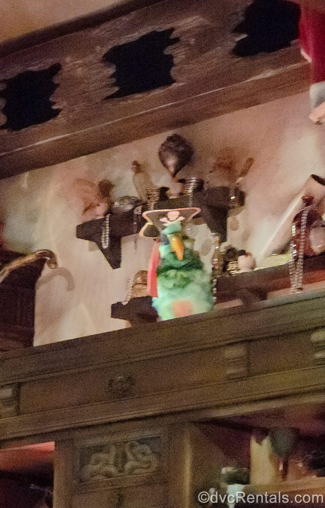 An animatronic of a green parrot in a pirate hat and eye-patch interacts with guests from his perch atop a shelf.