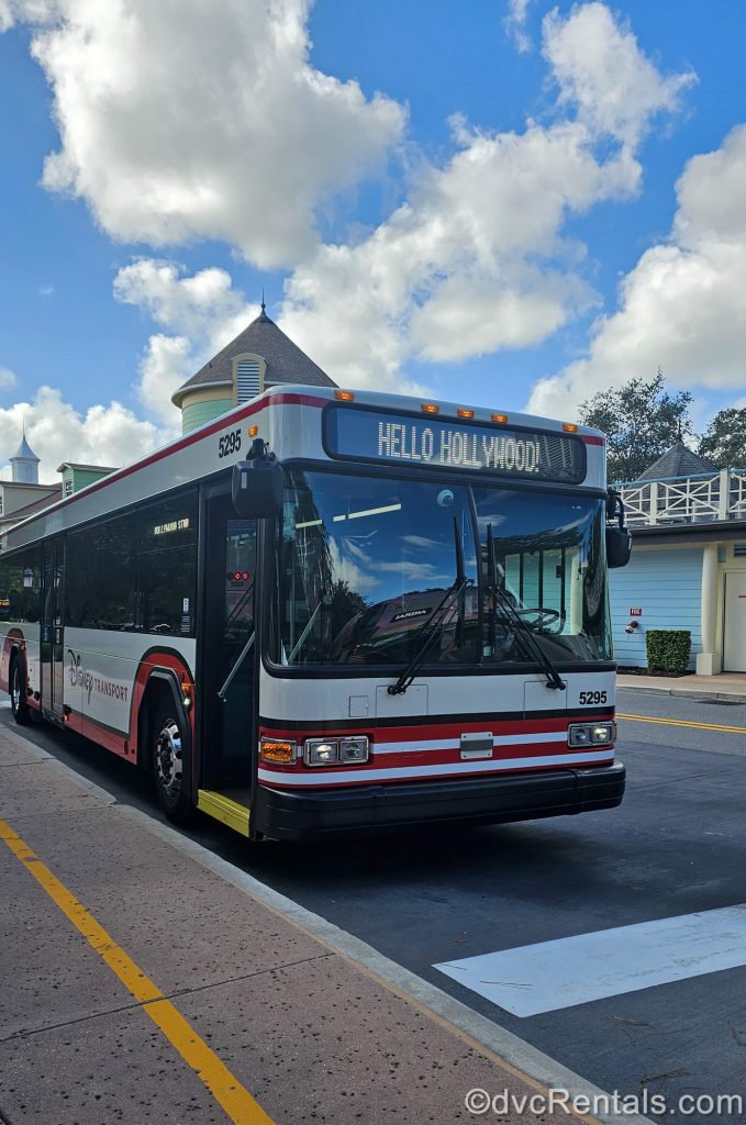 A red and white Disney Bus heading to Hollywood Studios pulls up to a stop at Disney’s Saratoga Springs Resort & Spa.