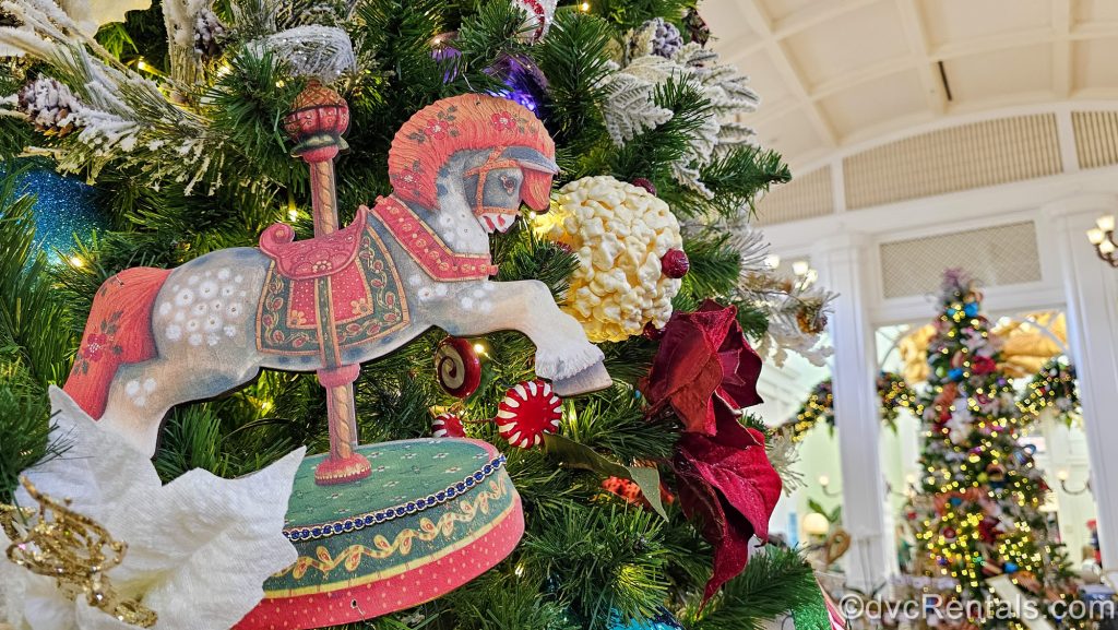 Carnival-themed holiday ornaments featuring carousel horses and popcorn adorn the Christmas trees displayed at Disney’s BoardWalk Villas.