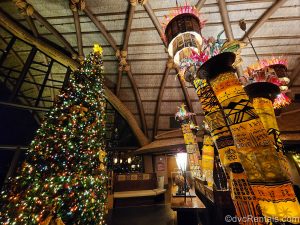 A very large Christmas tree decorated with African-inspired ornaments and red and green lights. It is displayed in the lobby of Disney’s Animal Kingdom Villas Kidani Village, along with other African art pieces and artifacts.