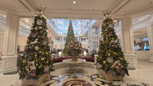 Three Christmas trees, each decorated with warm white lights and pastel Victorian-style ornaments are displayed in the lobby of Disney’s Grand Floridian Resort & Spa.
