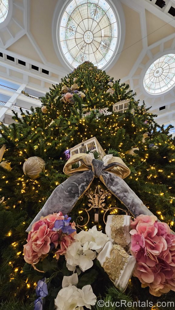 A giant Christmas tree is on display in the lobby of Disney’s Grand Floridian Resort & Spa. The tree is decorated with white lights, pastel flowers, and Victorian-style ornaments.