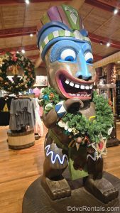 A tiki statue in a gift shop at Disney’s Polynesian Villas & Bungalows is decorated with a Christmas wreath. The wreath, along with others around the shop, is decorated with tropical flowers and shells.