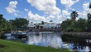 Disney’s Old Key West Resort is seen under a blue sky as a blue and yellow water taxi heads over the water to Disney Springs.