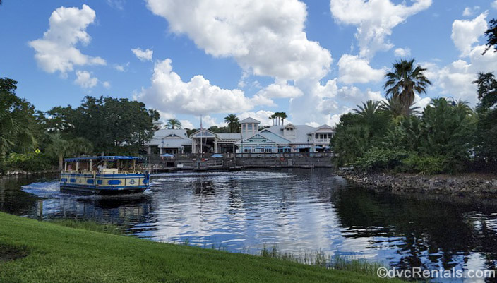 Disney’s Old Key West Resort is seen under a blue sky as a blue and yellow water taxi heads over the water to Disney Springs.
