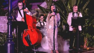A trio of musicians and a singer all dressed in glamorous formal outfits perform live outside the Tower of Terror attraction as part of the Twilight Soiree at the Tip Top Club during Disney Jollywood Nights.