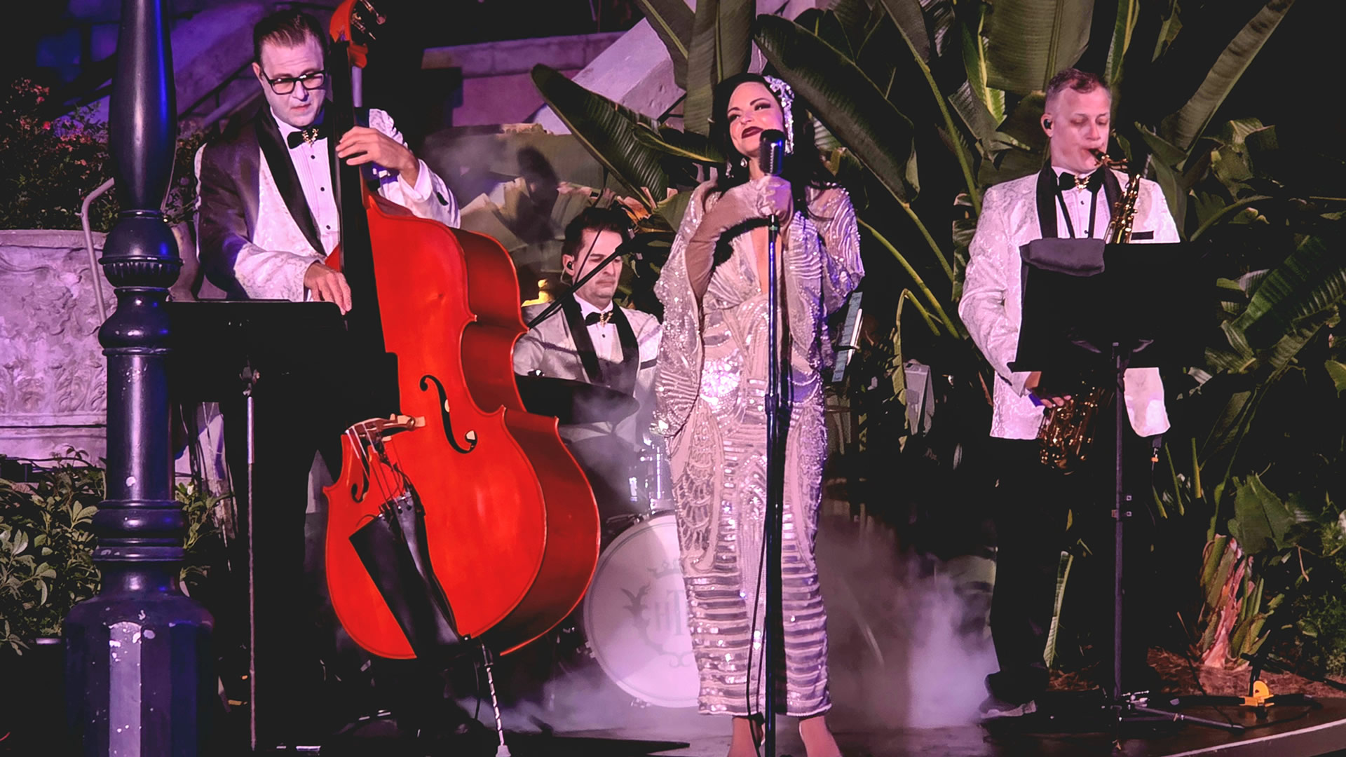 A trio of musicians and a singer all dressed in glamorous formal outfits perform live outside the Tower of Terror attraction as part of the Twilight Soiree at the Tip Top Club during Disney Jollywood Nights.