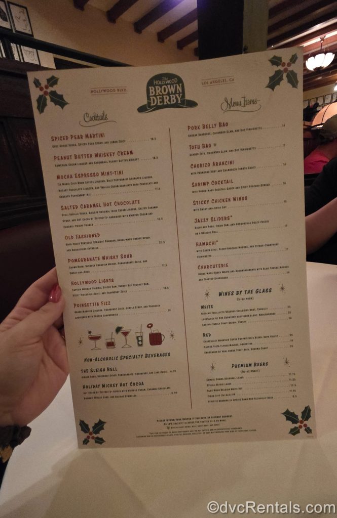 A hand holds up the menu for the food and drink offerings at Jazzy Holidays at the Hollywood Brown Derby during Disney Jollywood Nights.